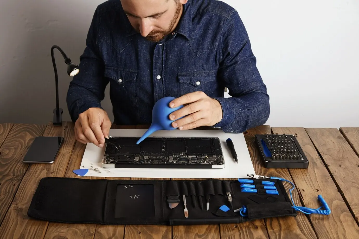 Ein Fachmann arbeitet in seinem Labor daran, einen Laptop zu reparieren und zu reinigen; in der Nähe befindet sich eine Werkzeugkiste mit speziellen Instrumenten.